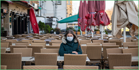 Coface Focus on Germany: More insolvencies in the pipeline. The photo shows a woman wearing a mask sitting alone on a café terrace in Cologne, Germany.